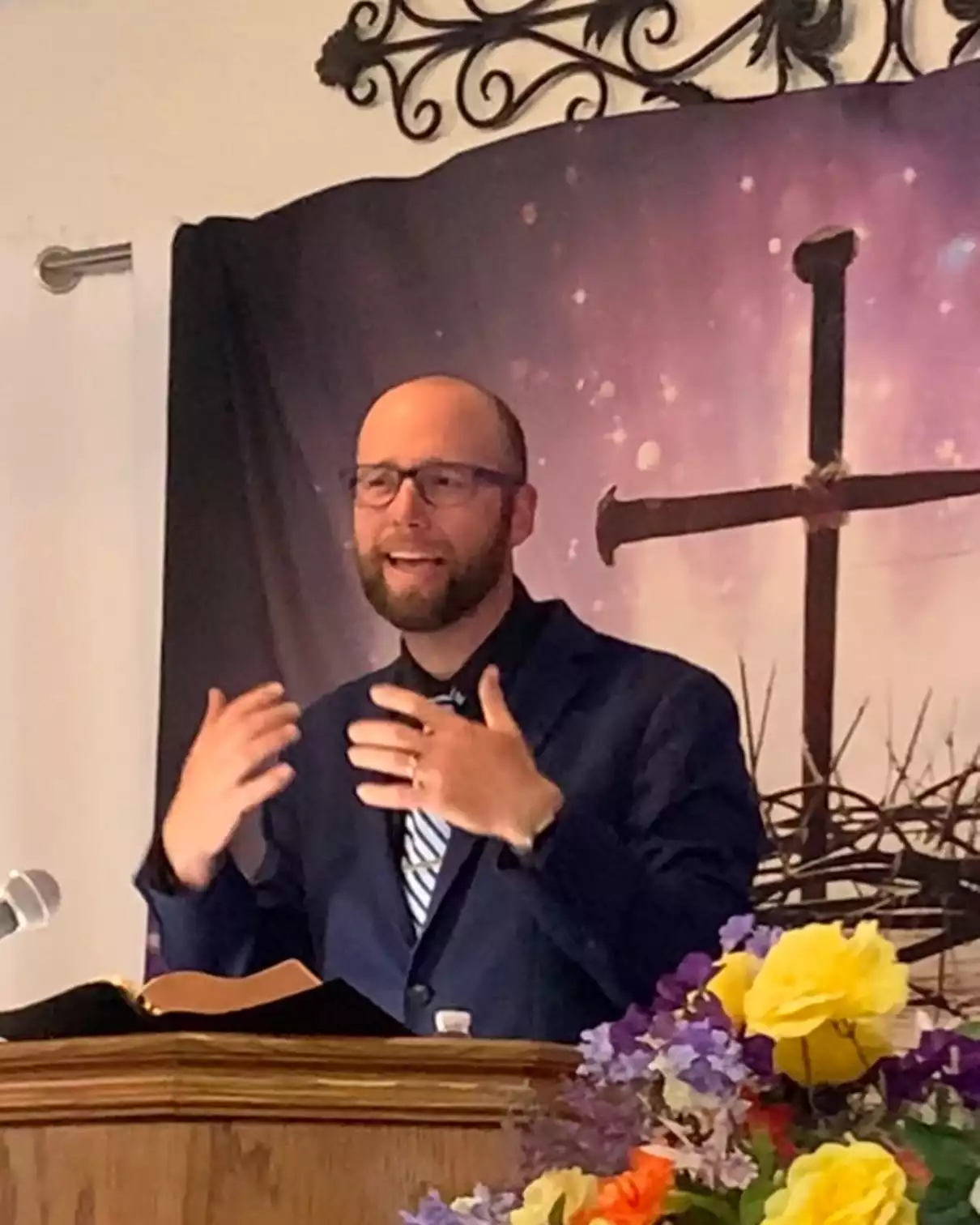 A pastor preaching from the pulpit in front of a cross banner at a Mid-Valley member church